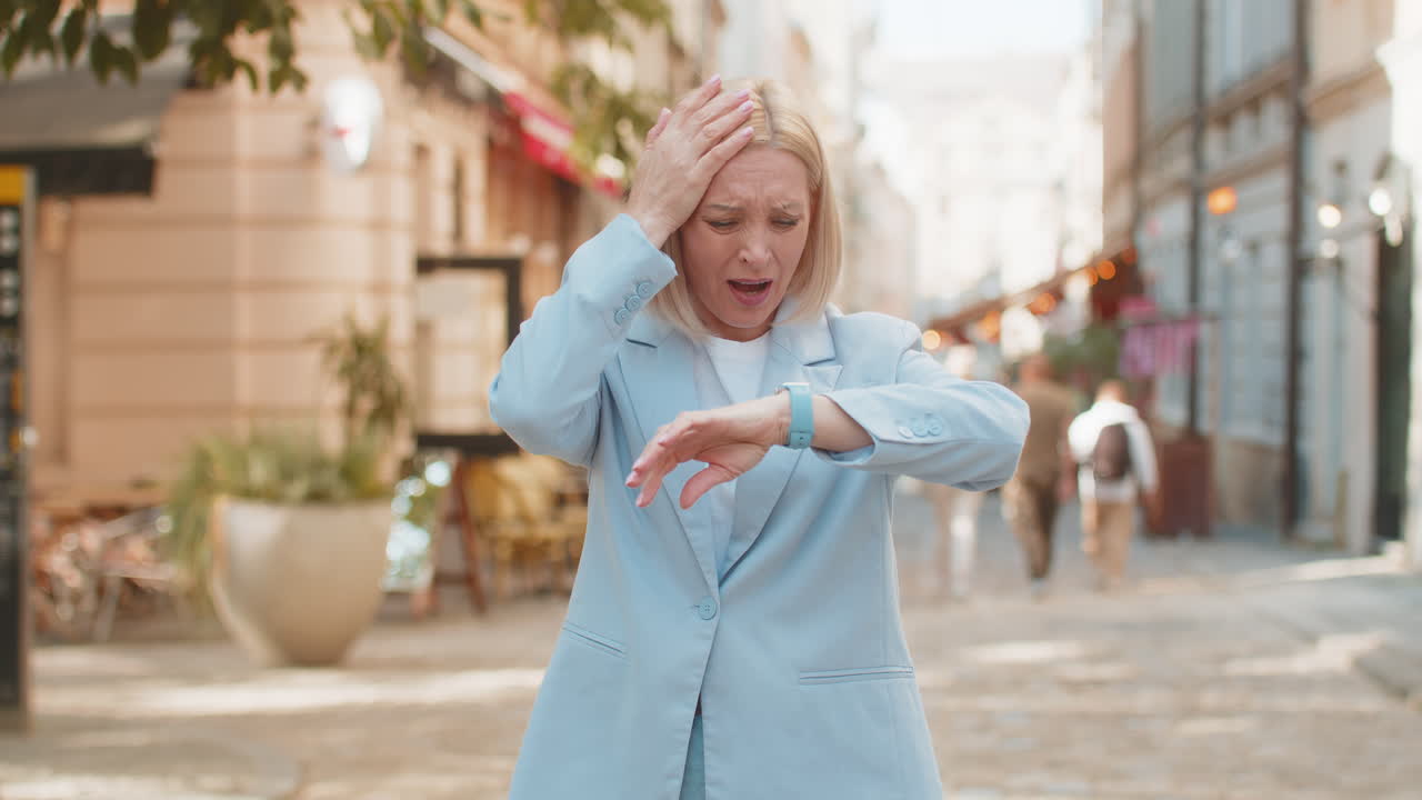 Shocked mature woman businesswoman in hurry checking time on smartwatch walking on city street