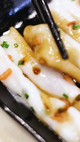 chopsticks lifting rice noodle rolls with sauce