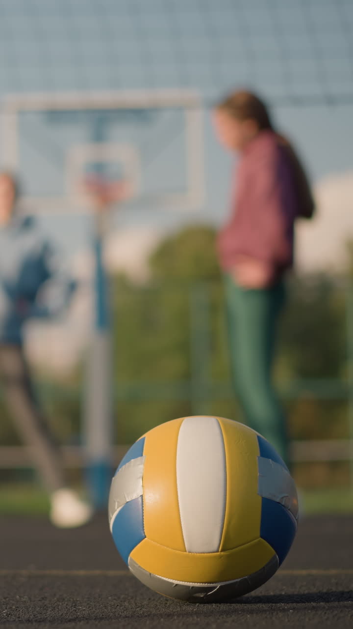 노란색 표시가 보이는 야외 스포츠 경기장에서 바닥에 놓인 배구, 배경에는 배구와 움직임에 초점을 맞추고 체력 운동에 종사하는 운동 선수