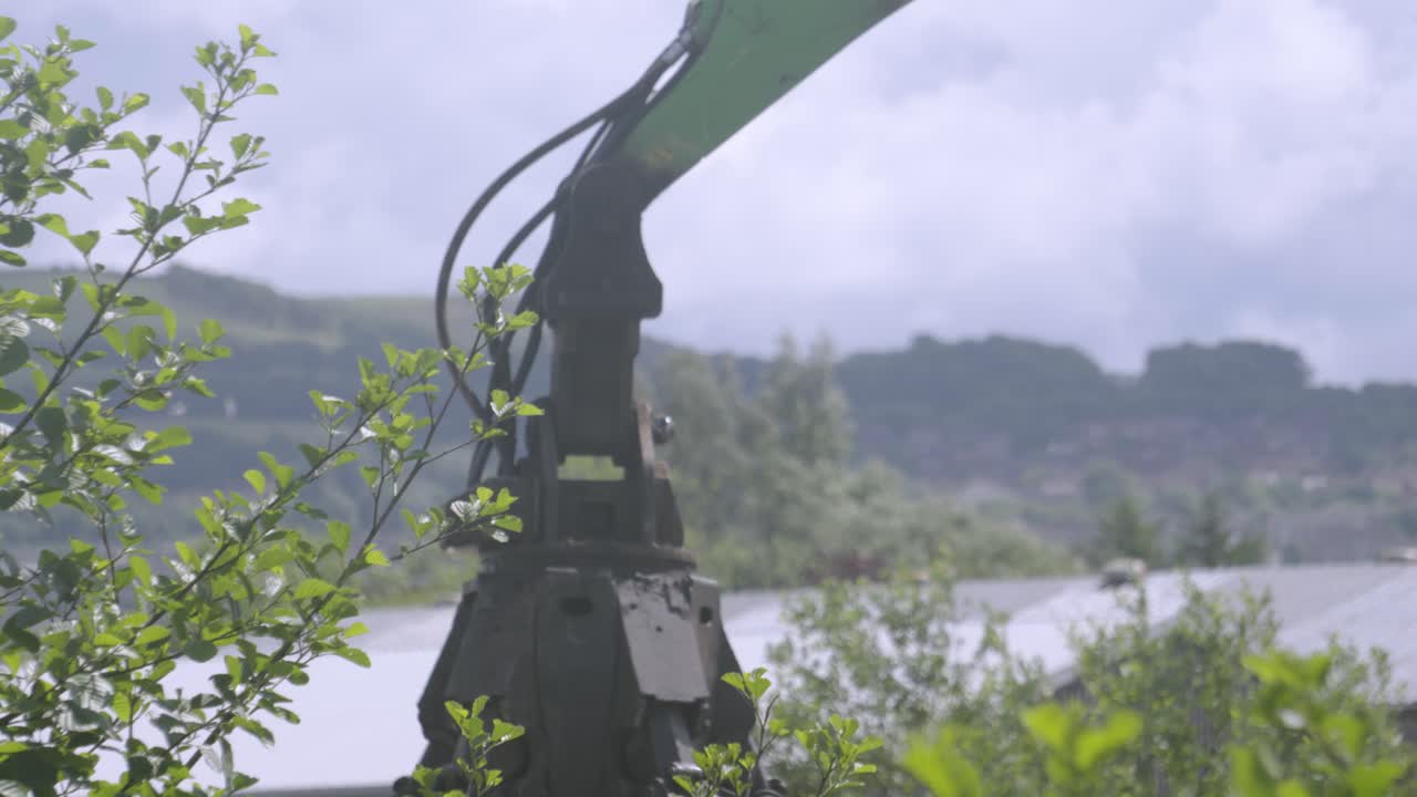 Giant Industrial Excavator Grab Machine Rising and Dipping After Picking Up Scrap Metal and Waste Junk Material with Warehouses in Background at Junkyard. Used for Disposing of Rubbish and Recycling.