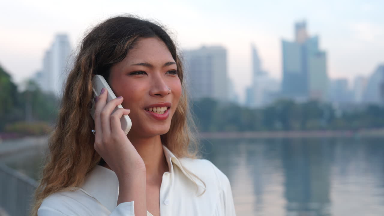 Young woman talking on the phone in a city park with a cityscape in the background