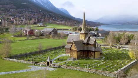 Beautiful-Wooden-Stave-Church-Of-Lom-Surrounded-By-Mountains-And-Trees-In-Norway---aerial-drone-shot