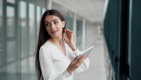 linda chica de pie con una tableta en el pasillo de cristal del centro de negocios