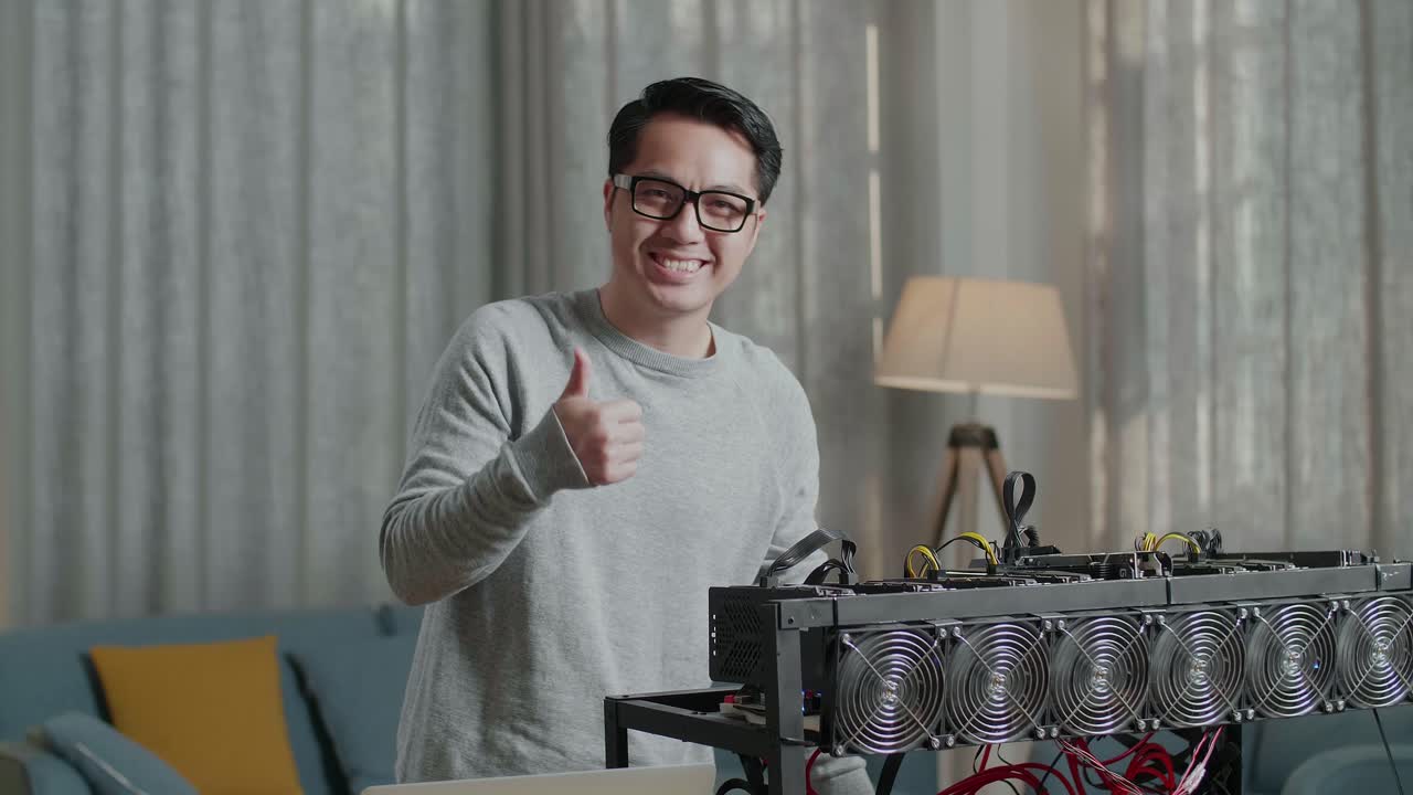 안경을 쓴 미소 짓는 아시아인 남자가 암호화폐를 채굴하는 노트북을 사용하는 동안 엄지손가락을 보여주는 제스처