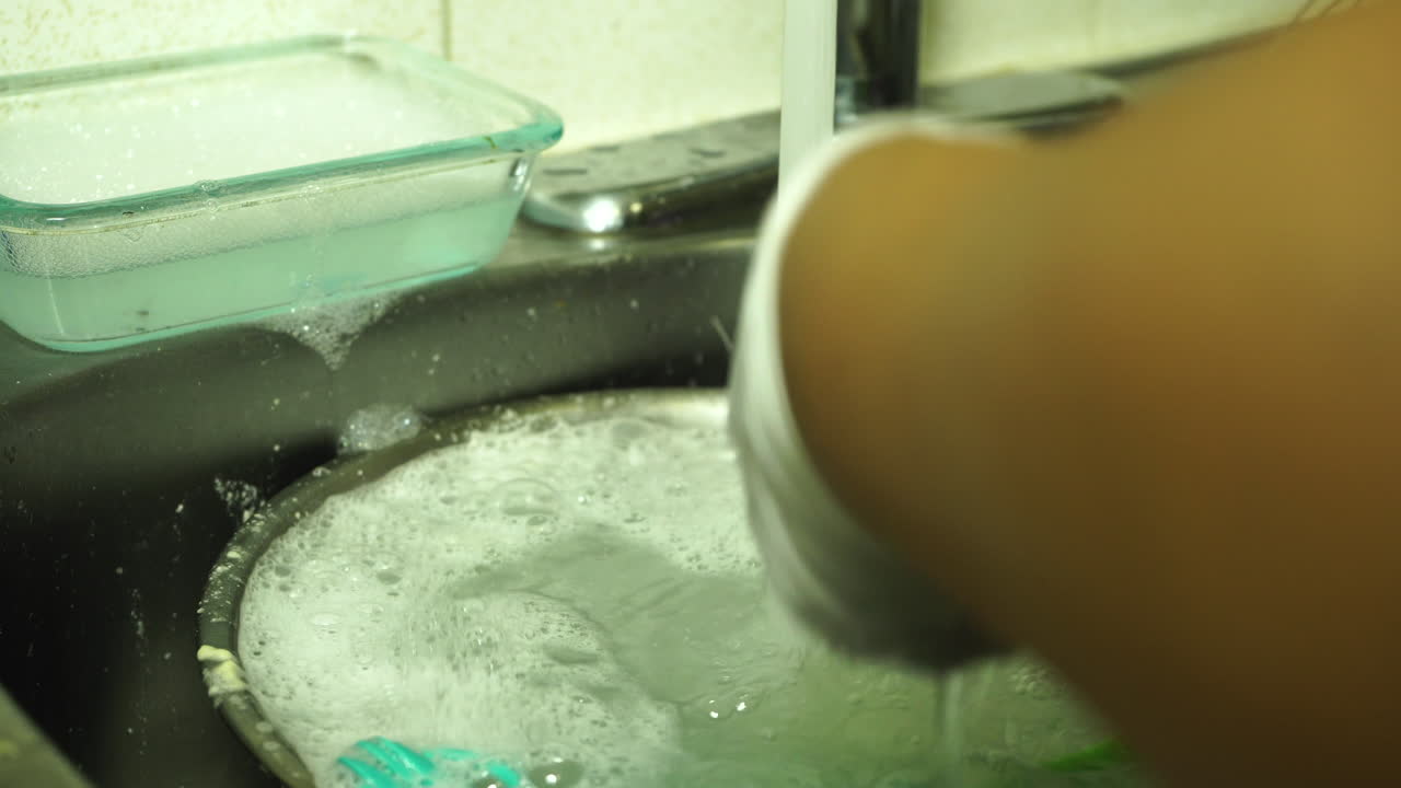 Persona che lava i piatti nel lavello sotto l'acqua corrente, contribuendo alla crisi idrica globale