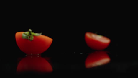 cut red tomato fall into 2 parts glass with water splashes in slow motion on a dark background