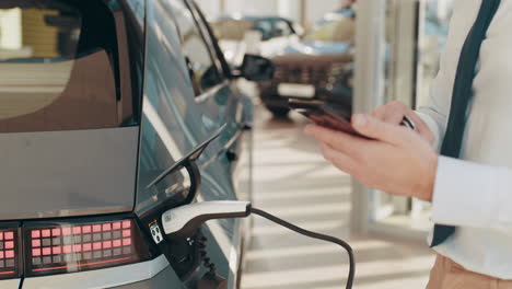 hombre de negocios usando un teléfono inteligente mientras carga un vehículo eléctrico