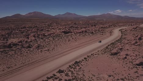 aerial view of a 4x4 on a dusty red road at the eduardo avaroa national andean wildlife reserve, slowly lifting the view to open up to the valley of rocks, "valle de rocas" in uyuni, bolivia