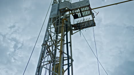metal tower with pipes and wires attached. low angle view on the oil rig at the backdrop of cloudy sky.