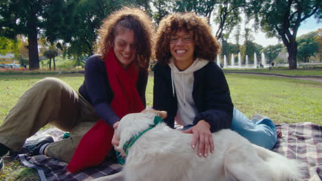 joyous girlfriends petting a dog and posing for camera in the park