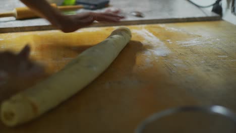 hands rolling and pressing cinnamon roll dough on wooden kitchen bench, filmed as close up handheld shot