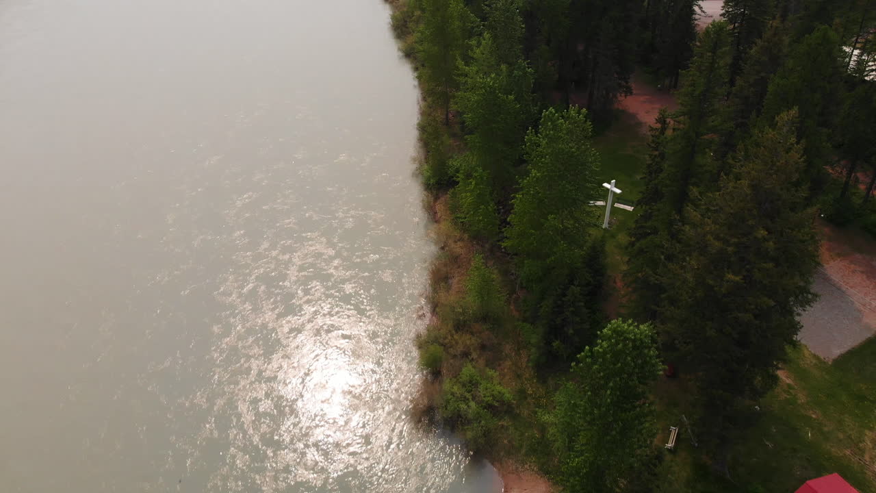 아침 해가 뜨는 동안 강과 숲이 우거진 은행의 항공 샷은 소나무 한가운데에 흰색 십자가를 드러내고 카메라는 천천히 아래로 이동합니다.