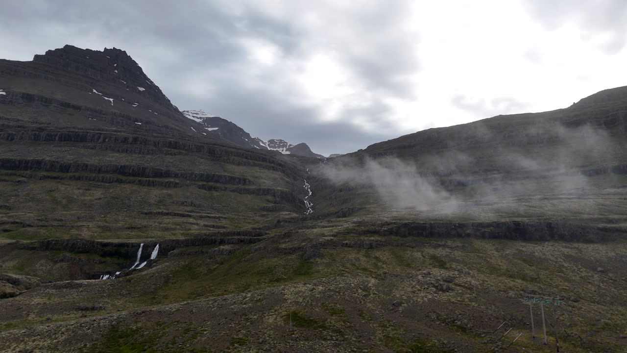 Misty mountain slopes and small waterfalls overlook Berufjörður as drifting clouds slide across the rugged Icelandic landscape