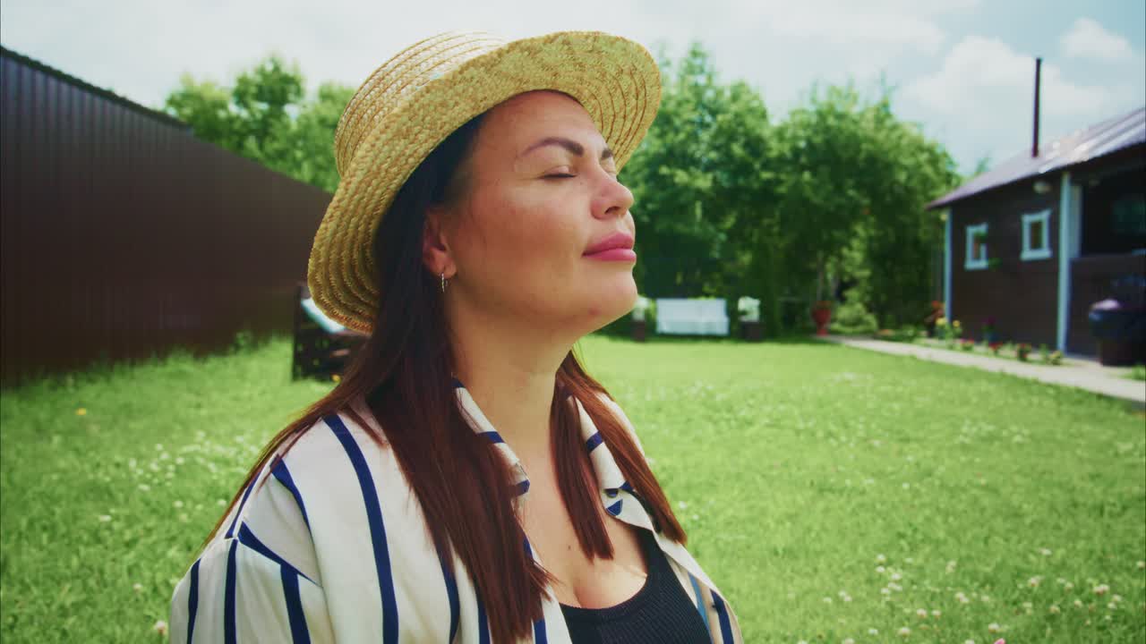 Woman enjoying sunny day outdoors with straw hat and relaxed expression in green garden