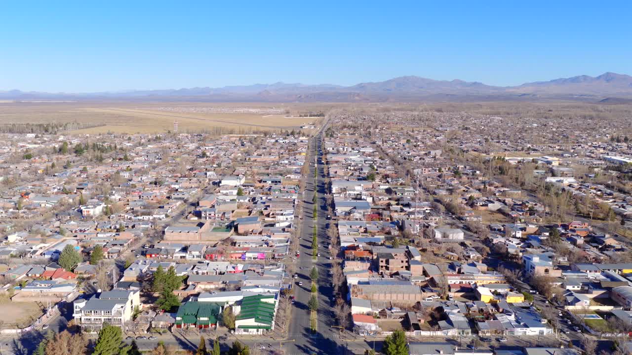 Descending drone view of Malargüe city layout with grid street pattern, arid terrain and Cordillera de los Andes mountain range on the horizon under clear skies in southern Mendoza, Argentina