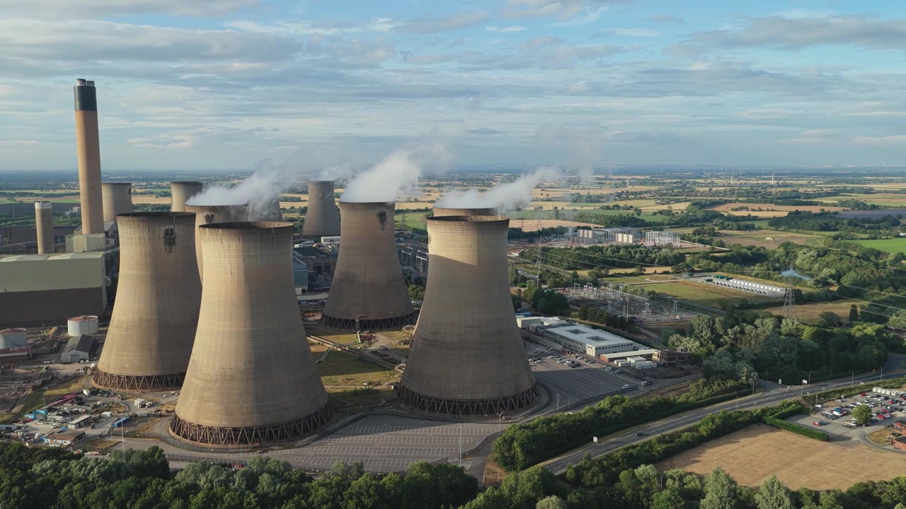 Grandi torri di raffreddamento industriali presso la centrale elettrica di Drax emettono nuvole di vapore bianco nel cielo in un pomeriggio soleggiato nella campagna inglese, mentre la produzione di energia continua nell'impianto.