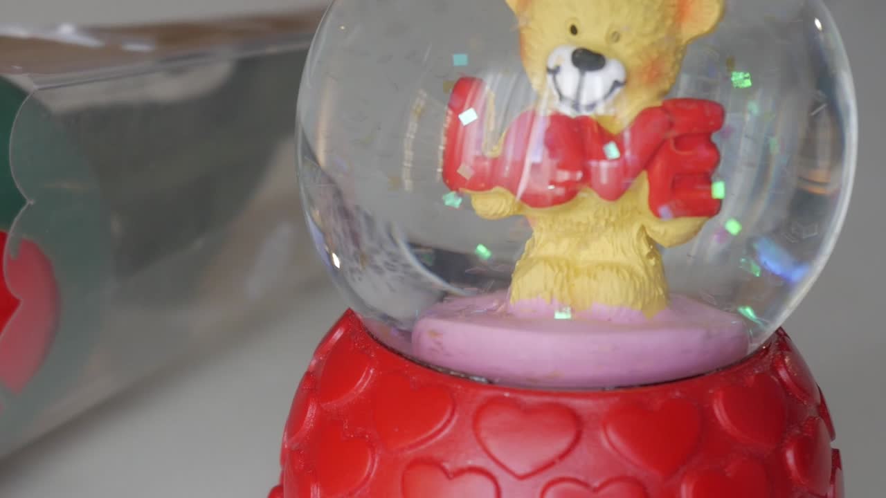 Cute teddy bear holding "LOVE" inside snow globe with pink base for Valentine's Day