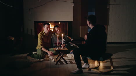 friends playing guitar around fireplace with wine and candles