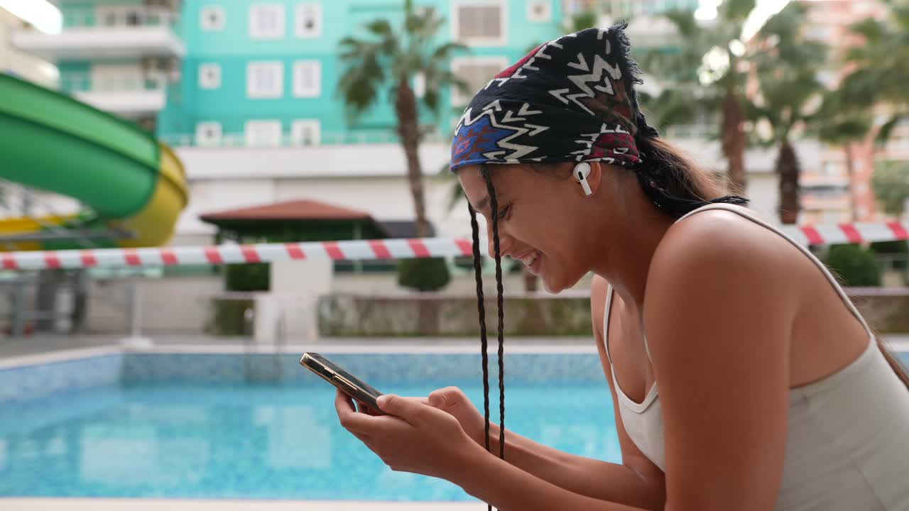 joven usando un teléfono inteligente junto a la piscina