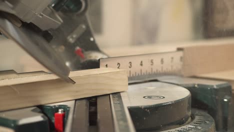 a front view of a miter saw cutting a work piece at a selected angle with sawdust flying. a hand is taking cut work piece