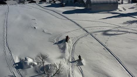 Aerial-of-snowmobile-towing-skier-who-jumps-over-small-hill-in-snowy-landscape