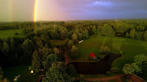 a reverse shot of a rainbow glowing at a green landscape with a forest and a small neighbourhood