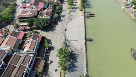 Drone-aerial-view-in-Vietnam-flying-over-Hoi-An-brown-color-river-canal-in-the-city,-small-brick-houses-and-wooden-boats-on-a-sunny-day