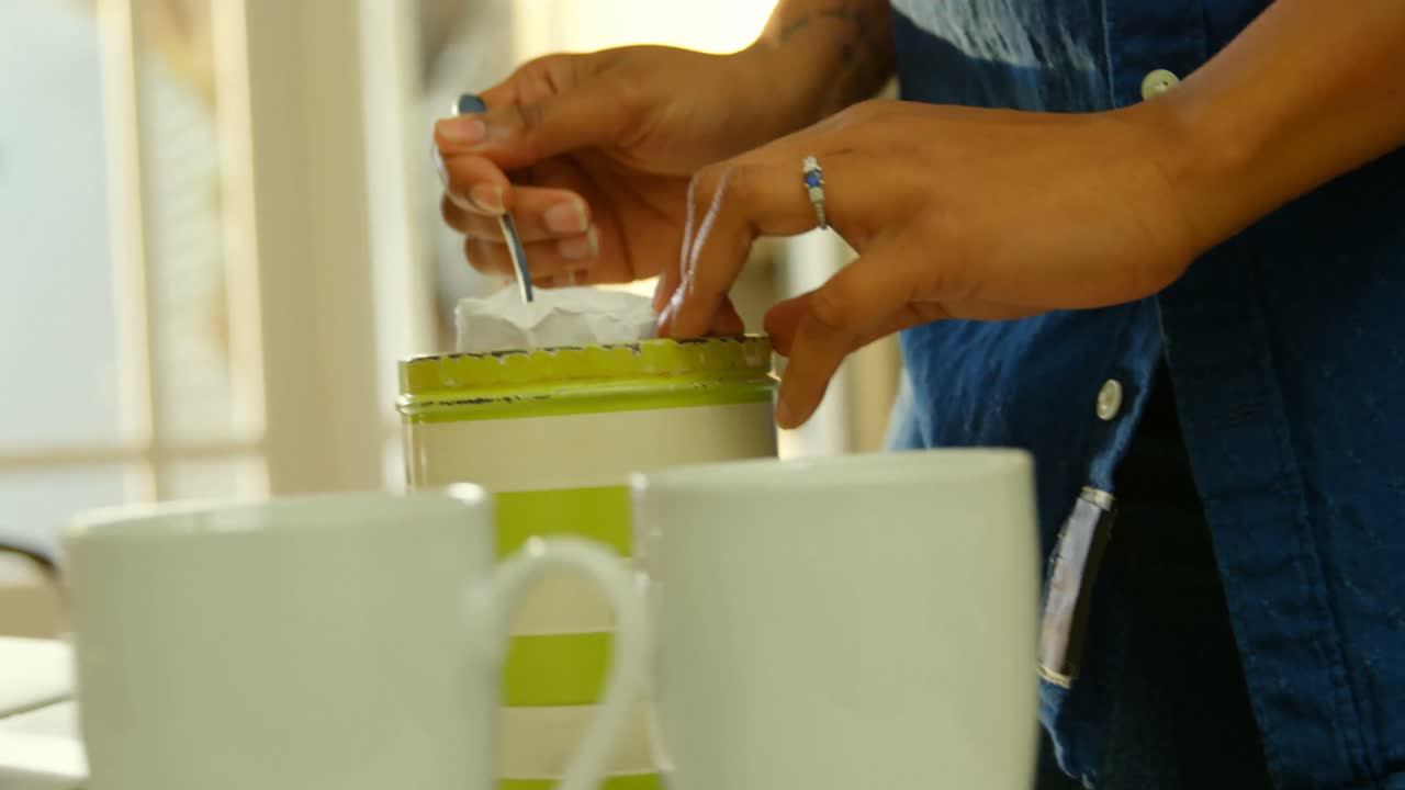 주방 4k에서 식탁 테이블에서 설탕 항아리에서 설탕을 취하는 젊은 흑인 여성의 중간 섹션