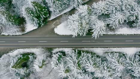 Siguiendo-Un-Camión-Rojo-Por-Un-Dron-Como-Vista-De-Arriba-Hacia-Abajo,-Conduciendo-A-Través-De-Una-Calle-Invernal-Cubierta-De-Nieve-Que-Conduce-A-Través-De-Un-Bosque-De-Coníferas