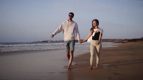 Pareja-Caucásica-Con-Ropa-Informal-Descansando-Relajarse-Tomados-De-La-Mano-Caminando-En-La-Luna-De-Miel-En-La-Playa.-Familia-Joven-Juntos-Gente-Feliz