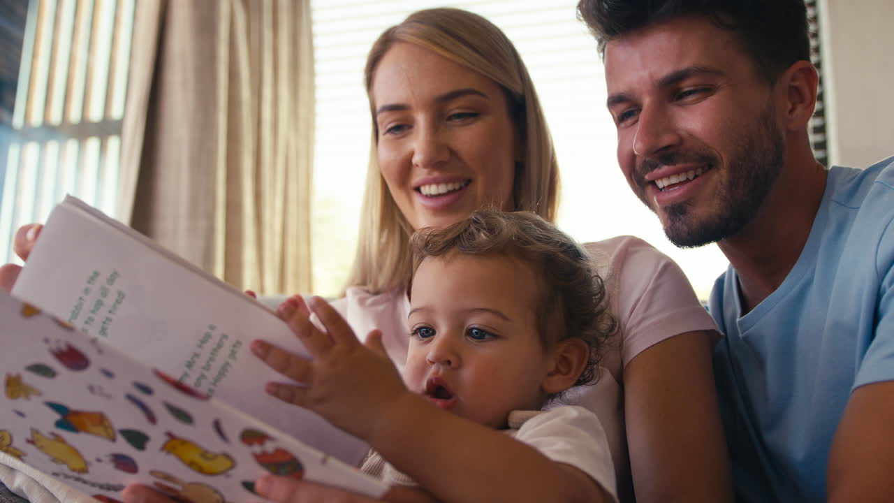 Famiglia seduta sul divano a casa con i genitori che leggono un libro con il figlio piccolo