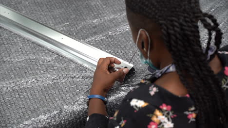 african american woman screwing a screw inside a metal rod on top of bubble wrap