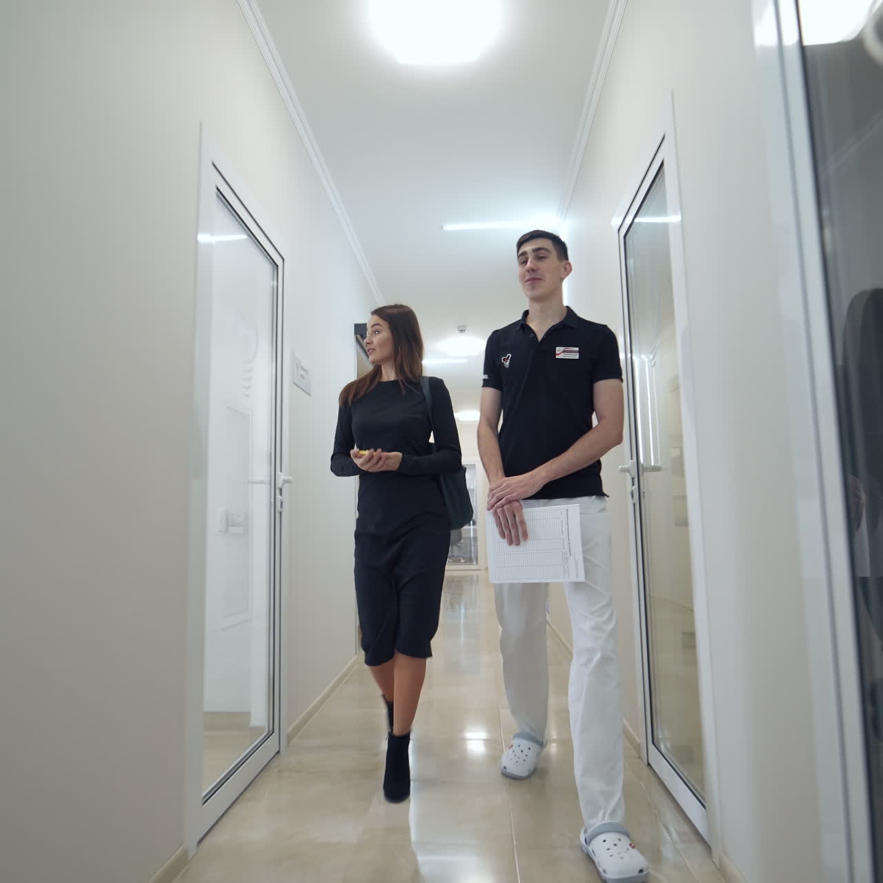 Health and dental care. Dental assistant with female patient going along the light corridor to the dental office. Pretty woman visits stomatologist.