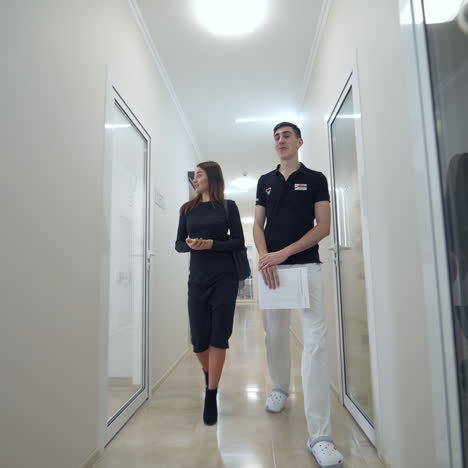 health and dental care. dental assistant with female patient going along the light corridor to the dental office. pretty woman visits stomatologist.