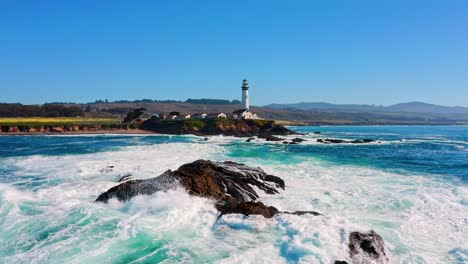 Waves crashing onto rocks near a lighthouse in the Pacific Ocean