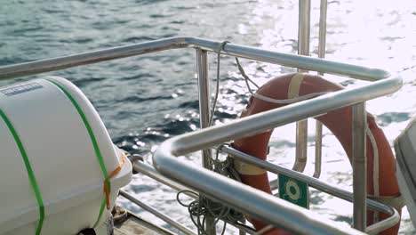 close up of a boat rail and life saver ring float while boat sails at sea