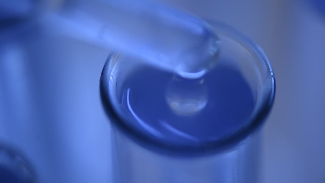 Pipeta goteando líquido transparente en un tubo de ensayo azul