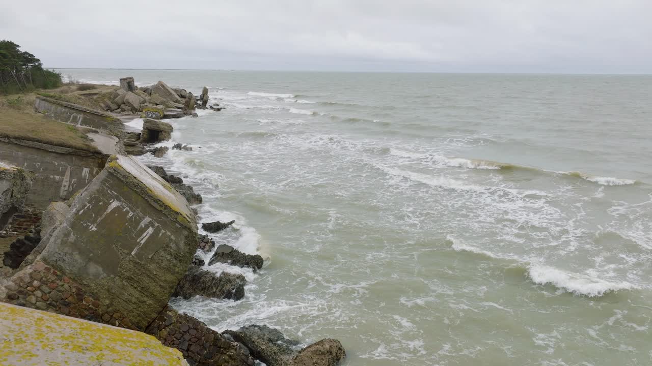 вид с воздуха на заброшенные приморские фортификационные сооружения в северных фортах кароста, побережье балтийского моря, большие волны, пасмурный день, замедленная съемка, беспилотник движется вперед