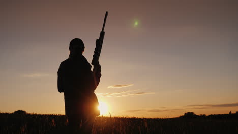 A-Female-Athlete-With-A-Gun-Looks-Ahead-At-The-Sunset-Women's-Sports-Shooting-Concept-Rear-View