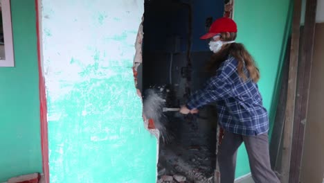 woman wearing face mask demolishing concrete wall using sledgehammer - medium shot