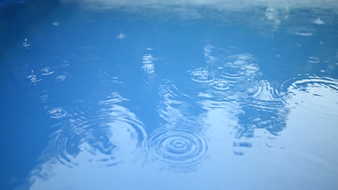 파란 물의 표면에 비방울의 원. 추상적인 배경. 수영장에서의 비.