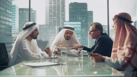 international business consultant advises on financial strategy plan to successful arab company owners. multicultural meeting in modern office between american and saudi businessman.