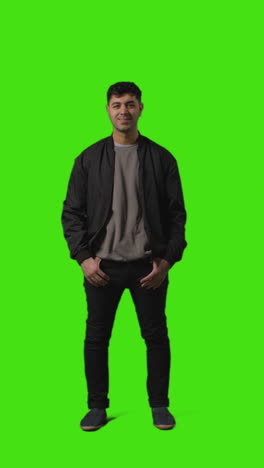 vertical video full length portrait shot of casually dressed young man standing against green screen