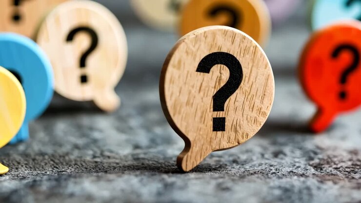 un signo de pregunta de madera en una burbuja de habla de madera rodeada de signos de pregunta coloridos
