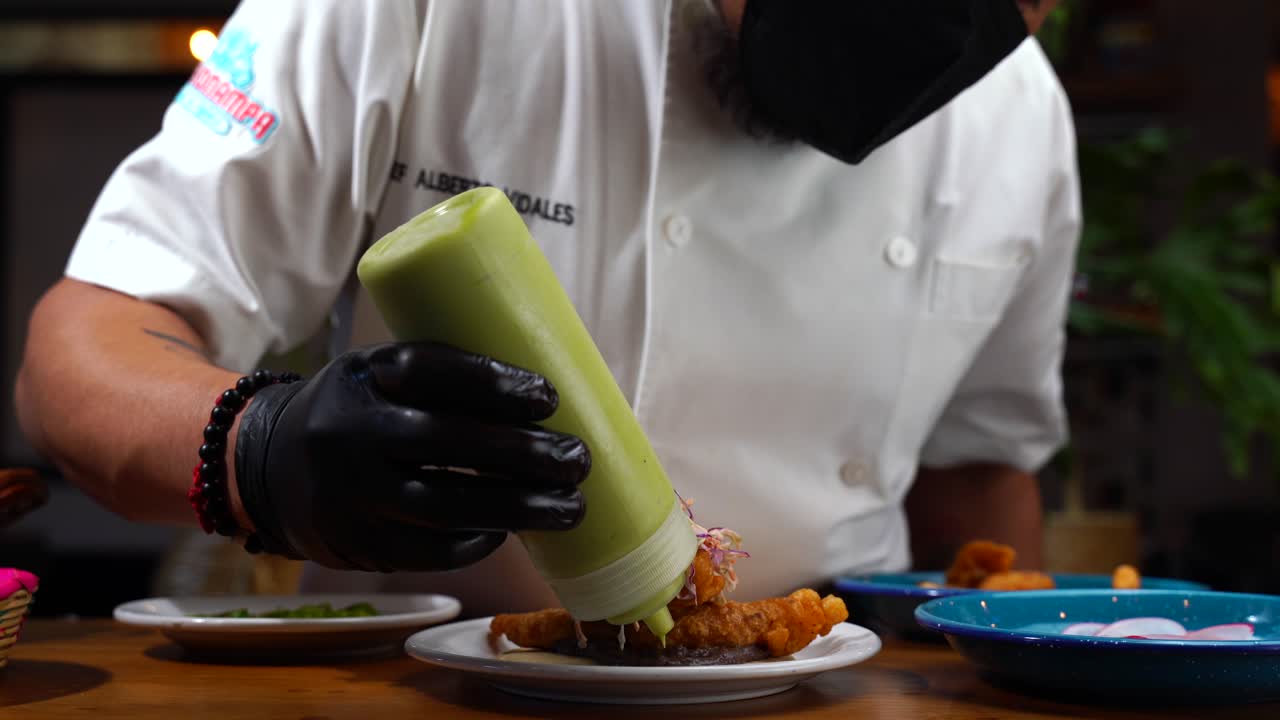 chef poniendo salsa aderezo mousse de aguacate guacamole taco de pescado mexicano estilo baja california