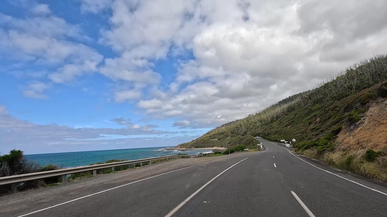 A 14-second video capturing a drive along the Great Ocean Road, showcasing coastal views, winding roads, and lush greenery under a partly cloudy sky