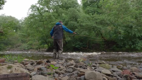 static shot of a fisherman fly fishing and casting into fast-flowing water wearing waders