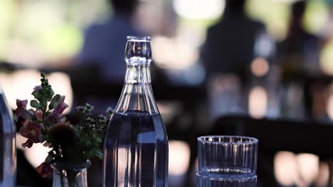 a clear glass bottle and a floral arrangement sit elegantly on a table with a blurred background.