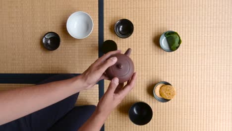 man shaking tea pot while seated on the tatami floor in a japanese house - closeup shot