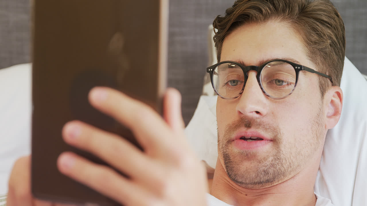 hombre sonriente con gafas acostado en la cama usando su tableta 4k 4k